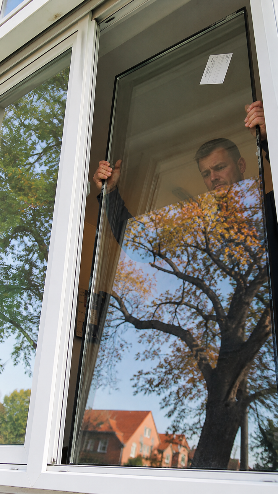 Monteur hält eine neue Glasscheibe vor dem Fensterrahmen